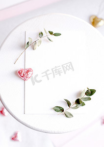 背景与白色桌子上的复制空间空白，上面有闪闪发光的心、桉树枝、花和叶子。