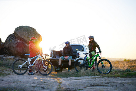 日落时在山上骑自行车后，朋友们正在皮卡越野卡车上休息。
