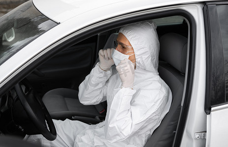 防护汽车摄影照片_身穿防护服、医用口罩和橡胶手套以防细菌和病毒的男子正计划开车。