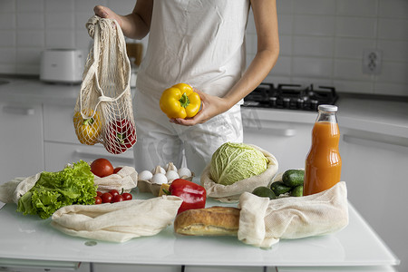 女人手拿着可重复使用的生态纺织品购物袋和蔬菜，取出红辣椒和黄辣椒。