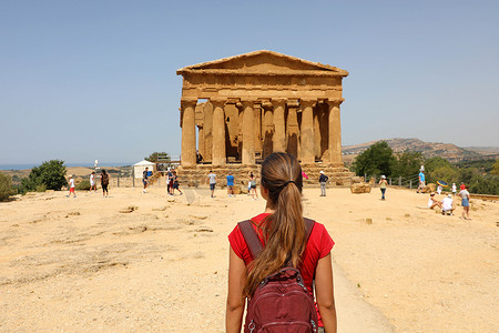 古代女摄影照片_女游客背着背包参观意大利西西里岛阿格里真托附近寺庙谷的康科迪亚寺