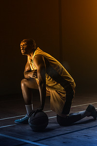 篮球运动员的肖像，膝盖放在地板上，一只手放在球上，向上看