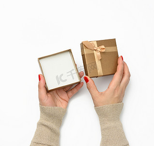 蝴蝶结摄影照片_两只女手拿着一个方形的金色礼盒，白色背景上有蝴蝶结，感恩的概念，生日