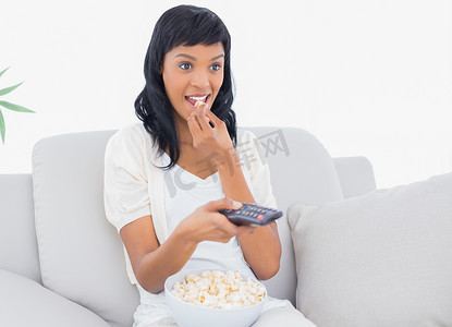 穿着白色衣服的黑发女性一边吃爆米花一边看电视
