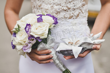 新娘手捧一束鲜花和两个结婚戒指。