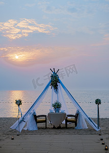 沙滩聚会摄影照片_恩爱的情侣在沙滩上享用浪漫的晚餐，点着蜡烛、灯笼和酒杯，欣赏美妙的日落