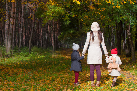 婴儿背影摄影照片_阳光明媚的日子里，年轻母亲和她可爱的小女儿在秋季公园散步的背影