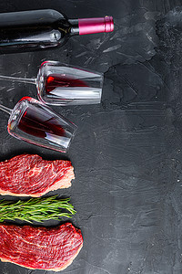 生的 picanha 牛排靠近瓶子和一杯红酒，黑色纹理桌面视图与文本空间。