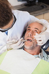牙医椅摄影照片_牙医在牙医椅上检查病人的牙齿