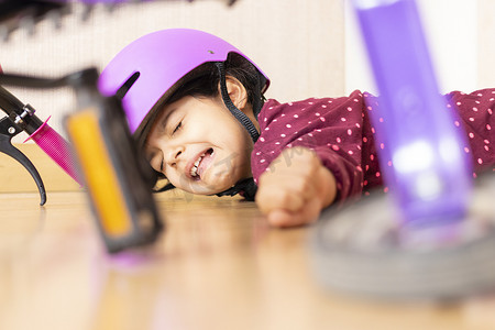 小女孩的哭泣摄影照片_伤心的小女孩在屋里玩自行车时摔倒在地
