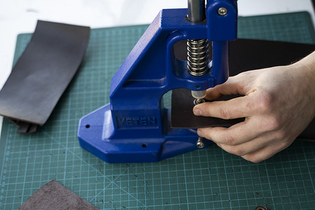 按扣女士钱包摄影照片_工匠使用手压机在皮革上设置按扣以制作钱包。