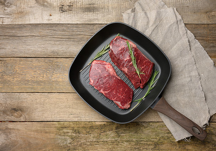 黑色方形烤盘中的两块生牛肉，木质背景中的牛排