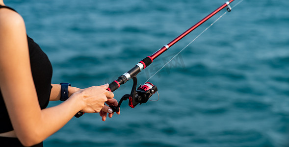 海面背景摄影照片_女人手拿着海面背景的钓鱼竿，在日落时钓鱼。