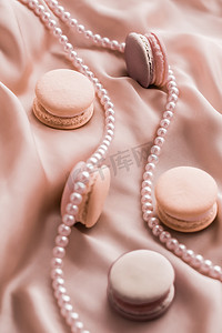 丝绸背景上的甜马卡龙和珍珠首饰、巴黎别致的珠宝、法式甜点食品和豪华糖果品牌的蛋糕马卡龙、节日礼物