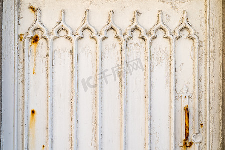 一扇白色木门的细节，上面有风化和生锈的油漆和哥特式窗户图案浮雕