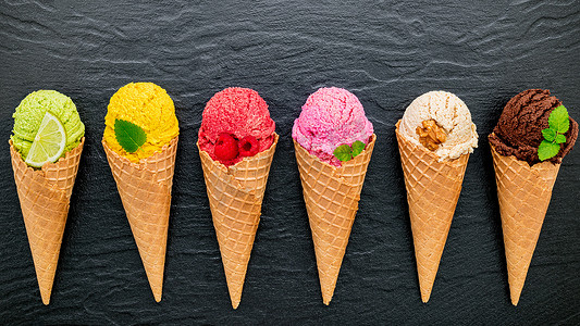 各种冰淇淋口味的锥体蓝莓、酸橙、开心果、杏仁、橙子、巧克力、香草和咖啡设置在深色石头背景上。