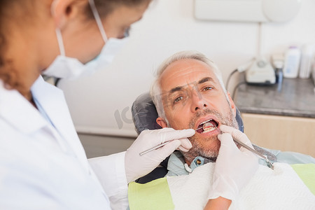 牙医椅摄影照片_牙医在牙医椅上检查病人的牙齿