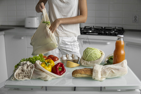 女人手拿着可重复使用的生态纺织品购物袋，里面装着蔬菜和水果。