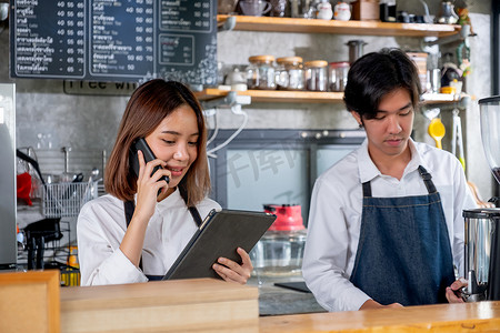 咖啡师女孩或咖啡机接听电话并记录订单，并站在咖啡店的同事旁边。