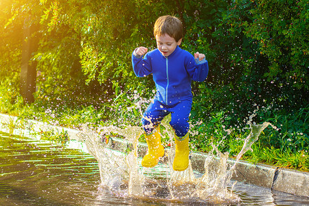 一个穿着橡胶靴的快乐男孩在水坑里跳跃。