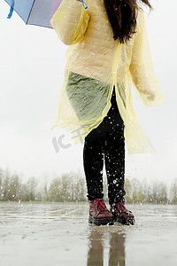 人在雨中摄影照片_女人在雨中玩耍，在溅起的水坑中跳跃