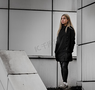 灰色建筑背景下金发黑衣的年轻女孩