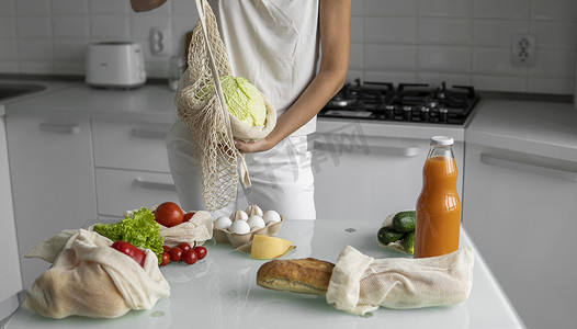 女人的手，拿着一个可重复使用的食品袋，在家里的厨房里放着蔬菜，把卷心菜拿出来。