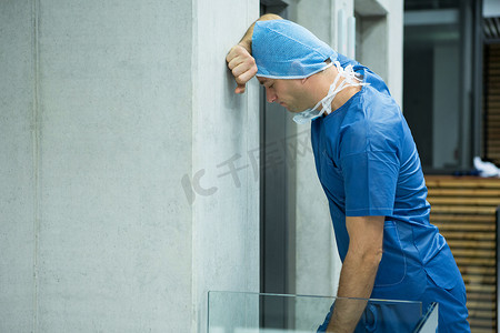 紧张的男外科医生靠在电梯附近的墙上