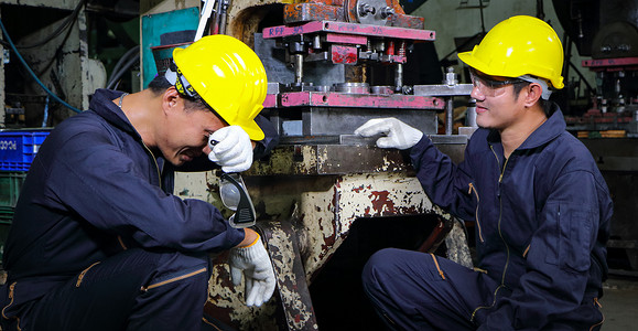 两名身着头盔制服的熟练亚裔工人正在讨论机器维修分析。