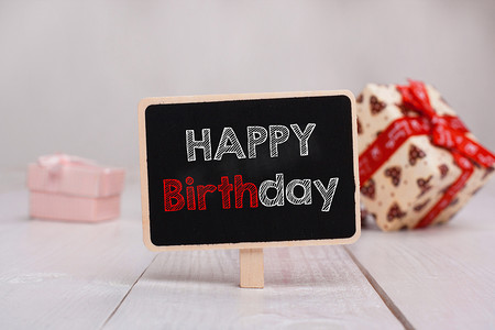 礼物盒框架摄影照片_黑色黑板，桌上有生日快乐文字，背景是礼物。
