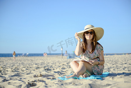 一个年轻的黑发女人在沙滩上放松的画像，正在阅读一本博