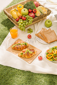 户外夏季或春季野餐的健康食品和配饰、带新鲜水果的野餐柳条篮、面包和露营自然背景中的一杯清爽橙汁。