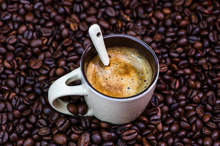 红色背景中带烤咖啡豆的咖啡杯，咖啡概念，特写咖啡照片