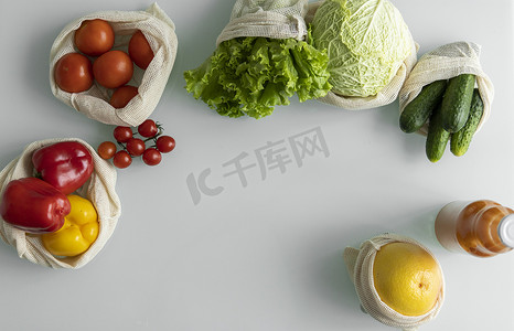 蔬菜、水果装在可重复使用的生态棉袋里，橙汁装在桌上的玻璃瓶里。
