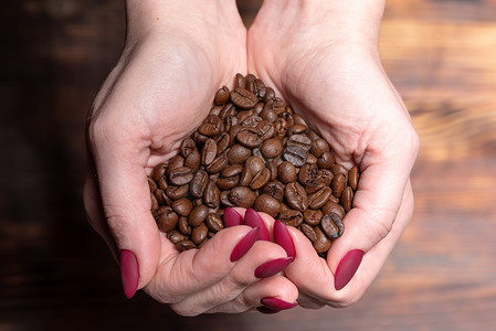 新鲜的烤咖啡豆从木制背景上的杯状女性手中倾泻而出