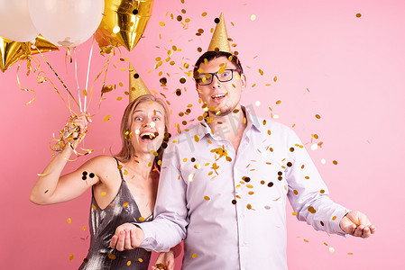 庆祝生日派对的快乐笑夫妇拿着金色气球和礼盒，扔金色纸屑