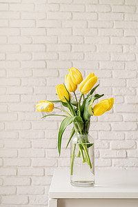 在一个玻璃花瓶的黄色郁金香在白色砖墙背景