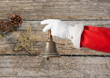 圣诞节金色铃铛摄影照片_拿着圣诞铃铛的圣诞老人的手
