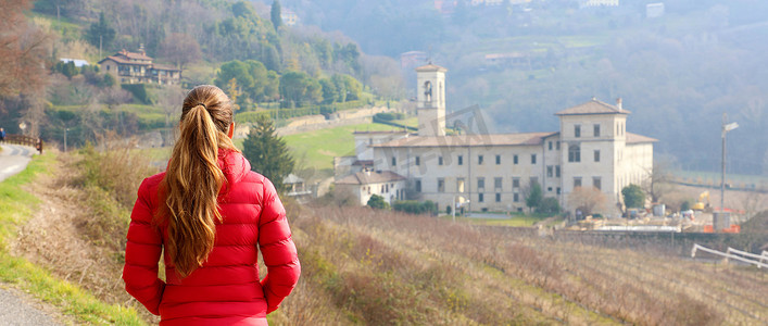 秋冬风景与年轻女子一起看阿斯蒂诺山谷和意大利阿斯蒂诺贝加莫修道院前修道院。