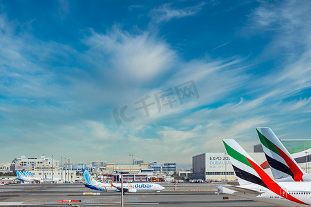 阿联酋迪拜 - CIRCA 2021：阿联酋迪拜 - CIRCA 2021：阿联酋航空公司和 FlyDubai 航空公司的飞机停在迪拜机场，背景是多云的天空。