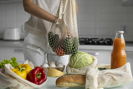女人手拿着可重复使用的生态纺织品购物袋，里面装着蔬菜和水果。