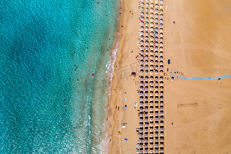沙滩鸟瞰图与五颜六色的遮阳伞，夏天日落时分，人们在海湾里用透明的蓝色海水游泳。