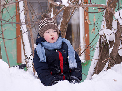 一个戴着针织帽、戴着围巾的男孩在冬天在雪地里玩耍。