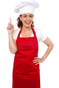 向上指示的美丽的微笑的女性厨师