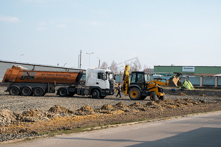 May摄影照片_LUTSK, UKRAINE - May 10, 2020：黄色轮式装载机挖掘机和卡车在建筑工地用沙子和砾石工作。