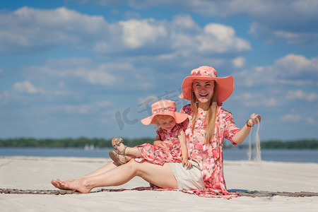 一个小女孩和她妈妈穿着相配的漂亮背心裙在沙滩上玩耍。