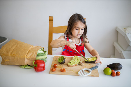 小女孩柠檬摄影照片_餐桌旁的小女孩在一片面包上撒鳄梨