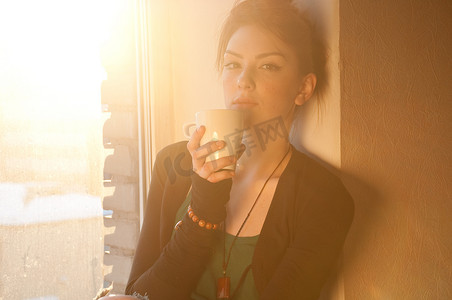 美丽的年轻女子，在太阳窗上端着一杯热咖啡