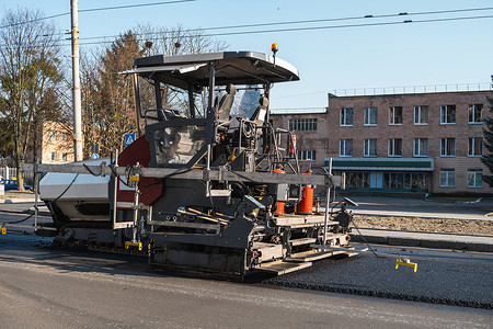 工业沥青摊铺机在街道道路施工现场铺设新鲜沥青。