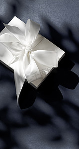 礼盒黑色摄影照片_黑色背景中带丝带和蝴蝶结的豪华假日白色礼盒、豪华婚礼或生日礼物